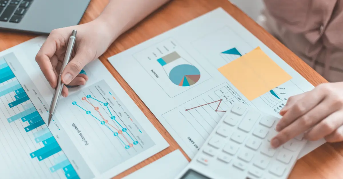 Ajánlat készítés menete. Egy hölgy számológépen számol a diagrammokon található adatok alapján.