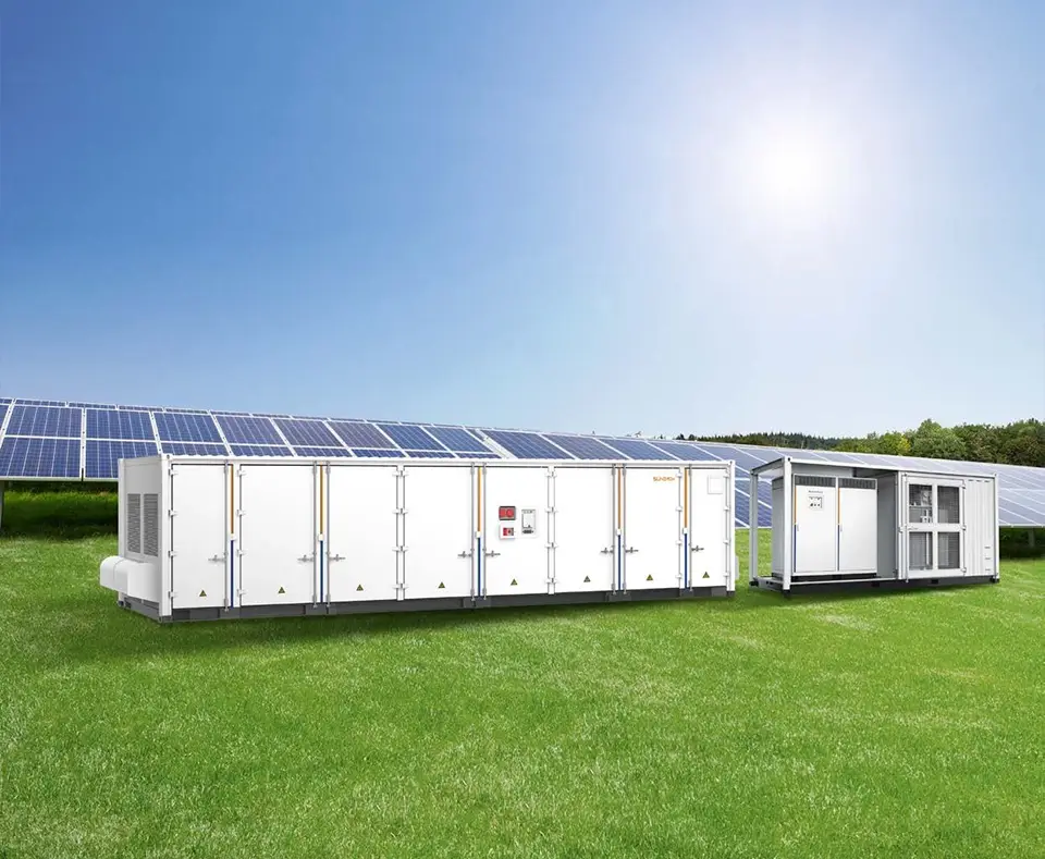 Nagy teljesítményű energiatároló egység egy zöld mezőn áll, háttérben egy működő napelem parkkal.